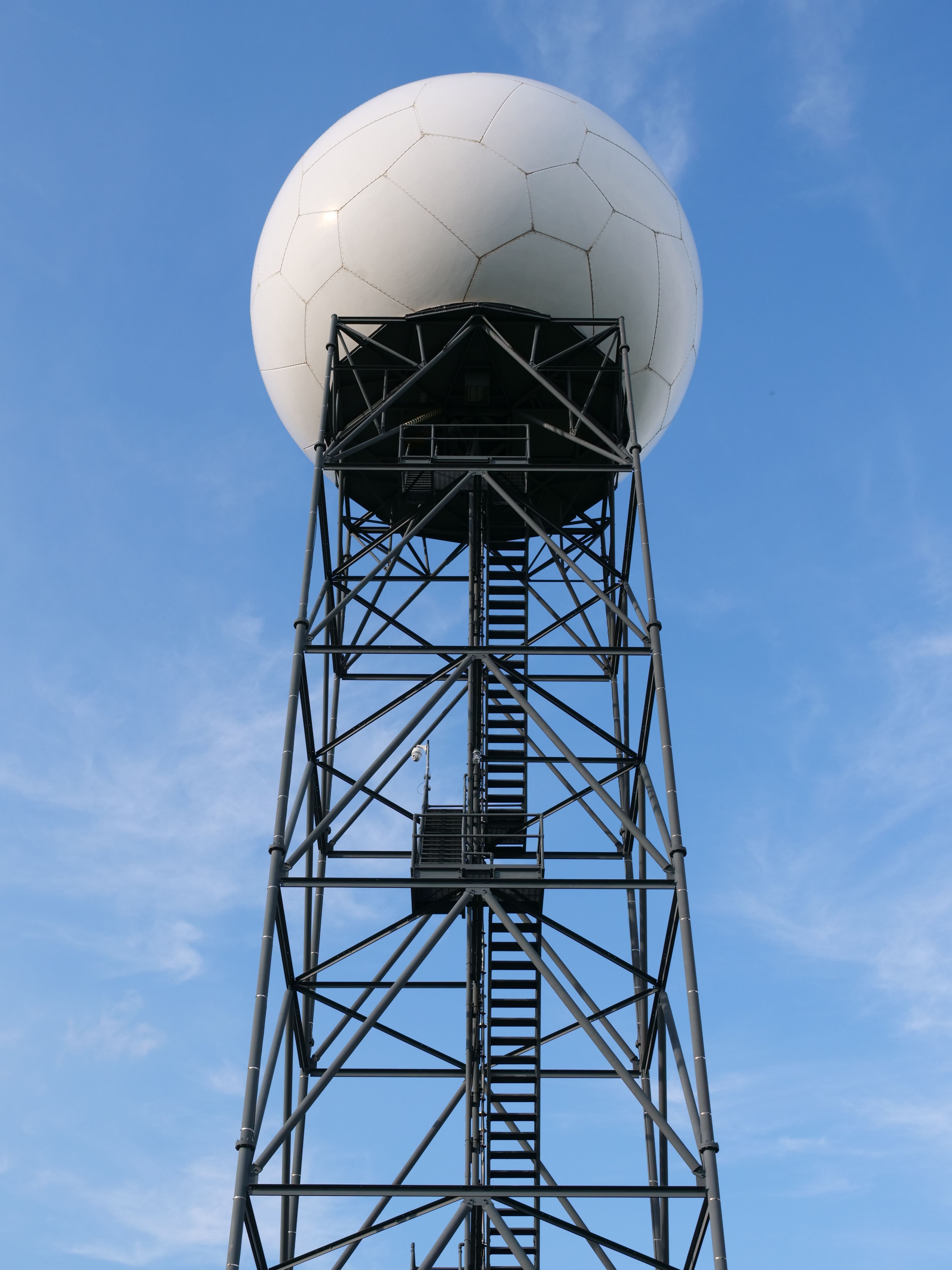 A tall radar tower with a geodesic dome against a clear blue sky, showcasing industrial architecture.