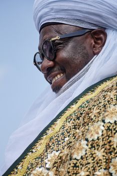 A man wearing traditional African garments, smiling and looking to the side.