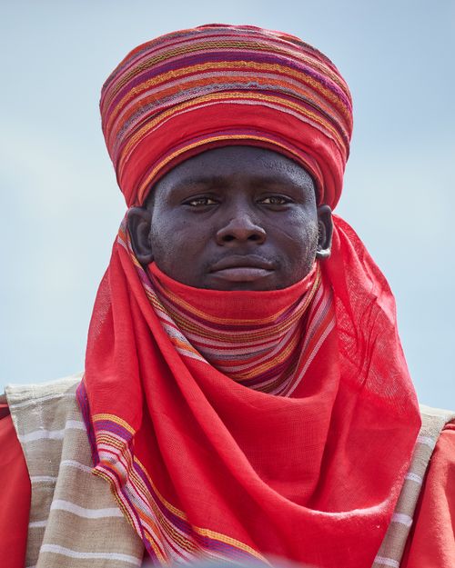 Free Close-up portrait of a man wearing vibrant red traditional African clothing against a clear sky. Stock Photo
