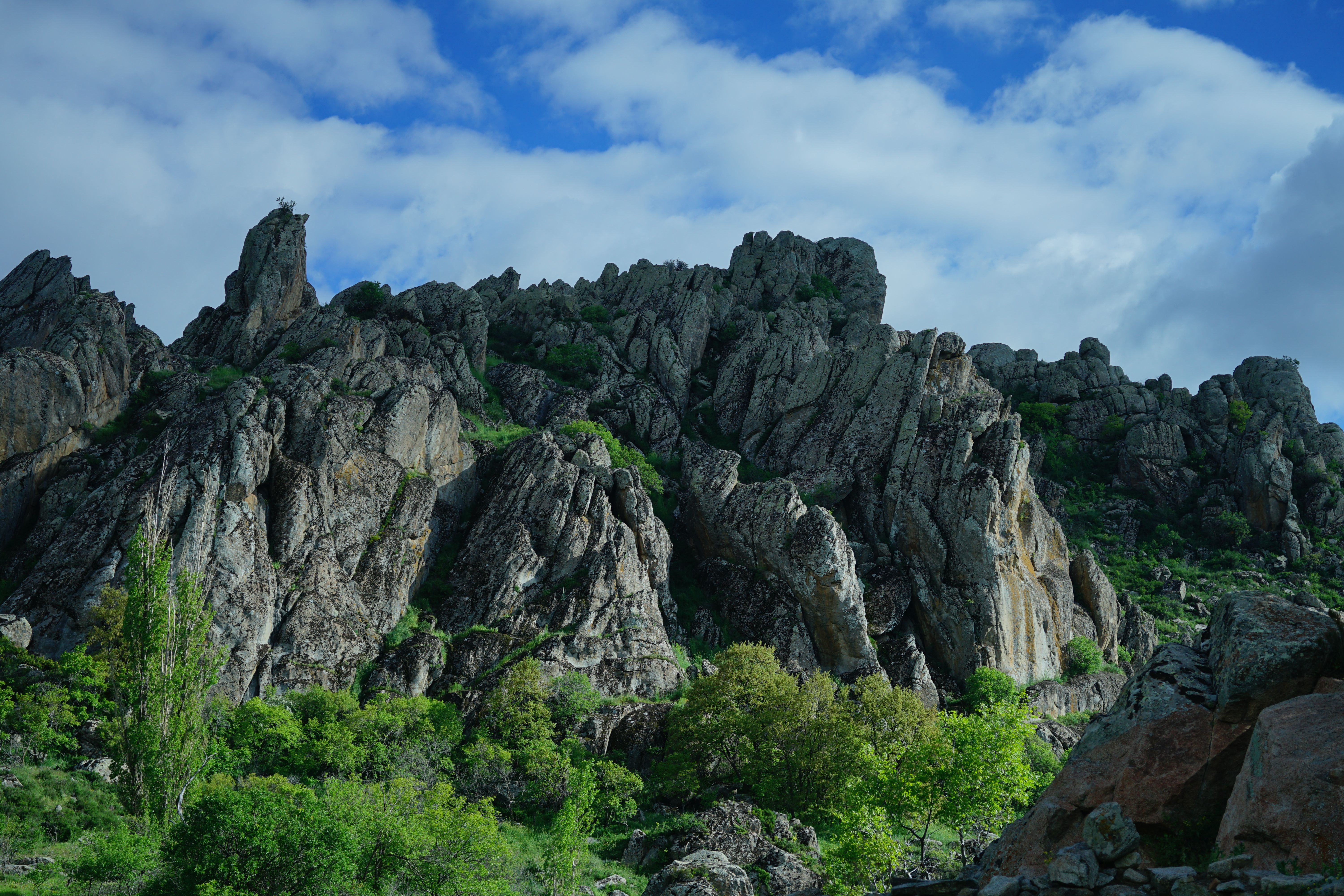 Mountain landscape with rocky cliffs and lush greenery under a vibrant blue sky.