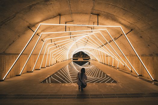 A solitary figure kneels in a geometrically lit tunnel, creating a mesmerizing reflection.