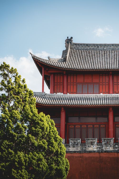 Free Red temple with intricate roof design set against a blue sky and lush greenery. Stock Photo