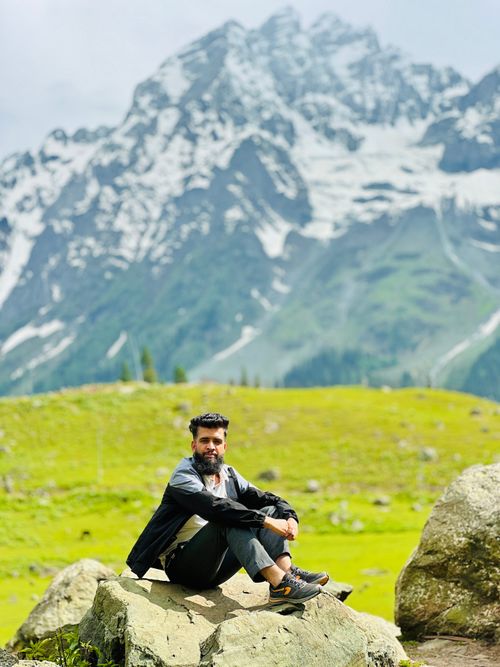 Free A man sitting on a rock with a picturesque mountain backdrop, capturing the essence of adventure and tranquility. Stock Photo