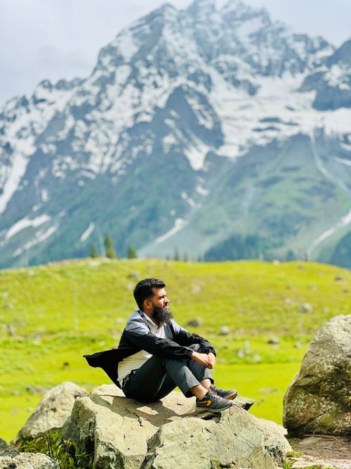 Free A man sitting peacefully on a rock, enjoying breathtaking mountain scenery. Stock Photo