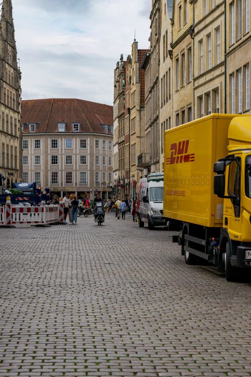 Free Lively street in Münster with people, cyclists, and delivery trucks on a cobblestone road. Stock Photo