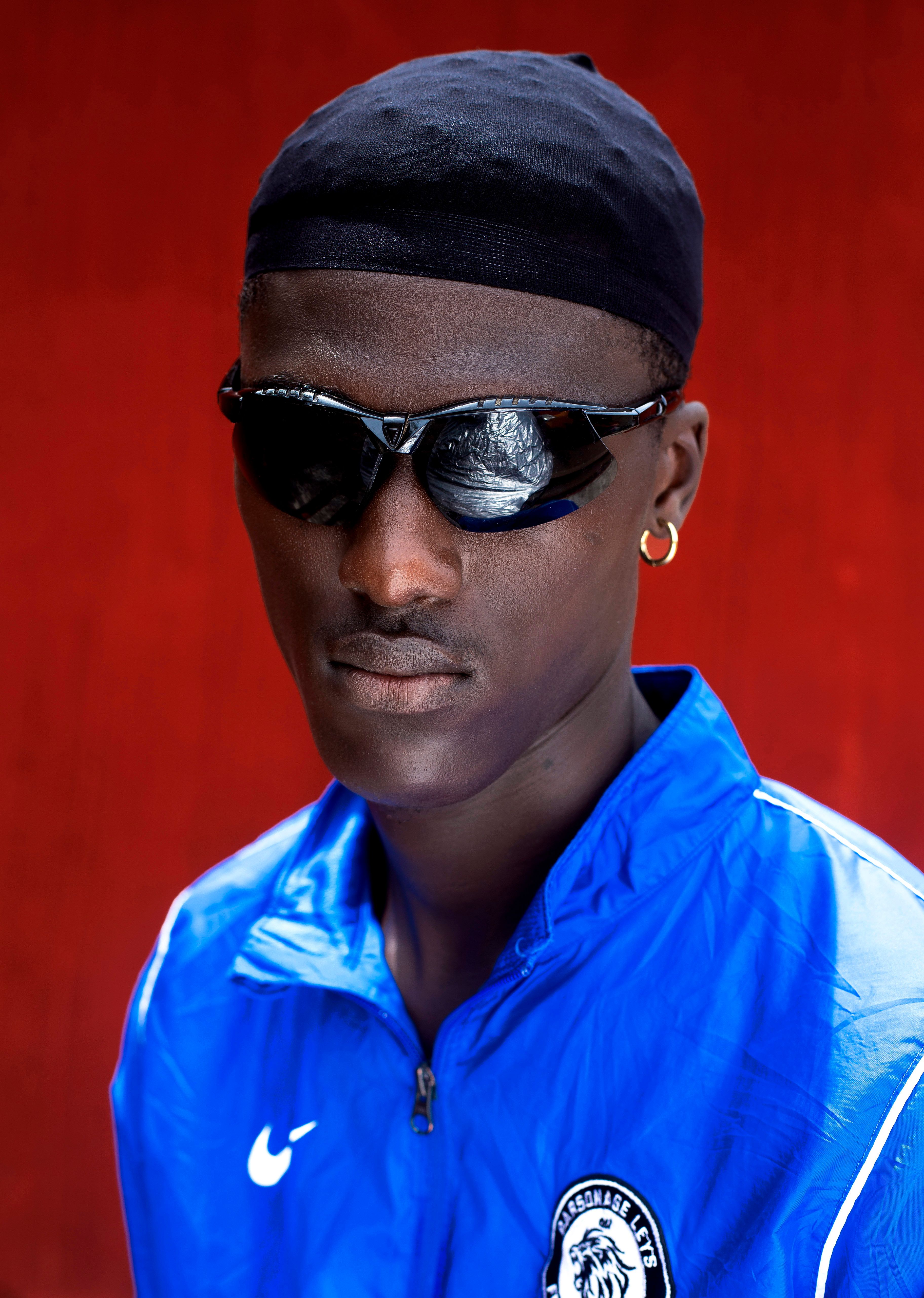 Stylish portrait of a young man wearing sunglasses and a blue sports jacket against a red background.