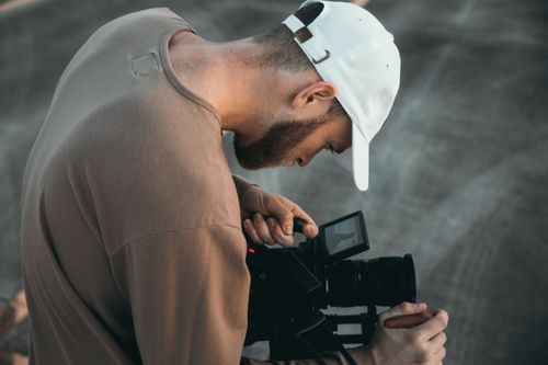 Free Man focusing on camera setup for an outdoor video shoot, showcasing precision and dedication. Stock Photo