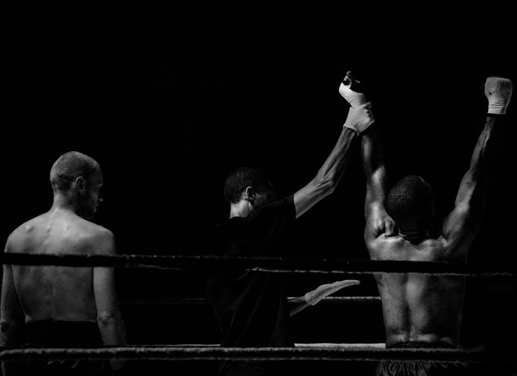 Grayscale Photography of Man Holding Boxer's Hand Inside Battle Ring