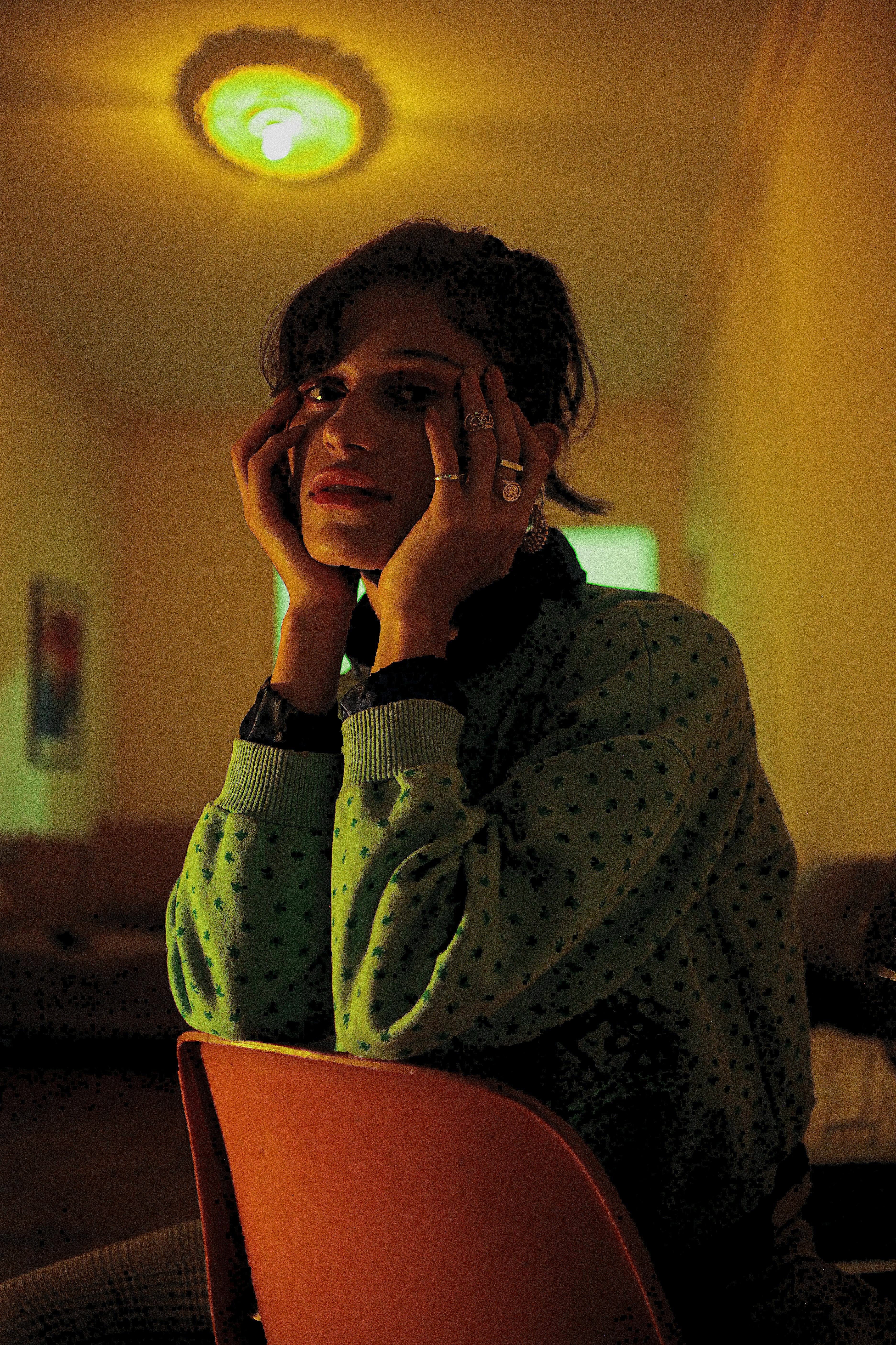 A woman in a cozy dimly lit room sits pensively, surrounded by warm ambiance.