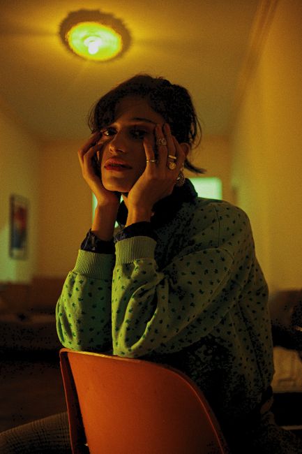 A woman in a cozy dimly lit room sits pensively, surrounded by warm ambiance.