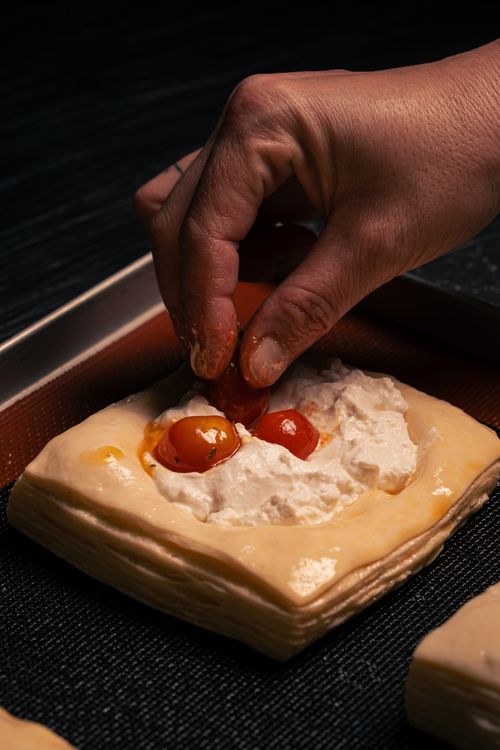 Free Close-up of hand placing tomatoes on savory cheese pastry for baking. Stock Photo