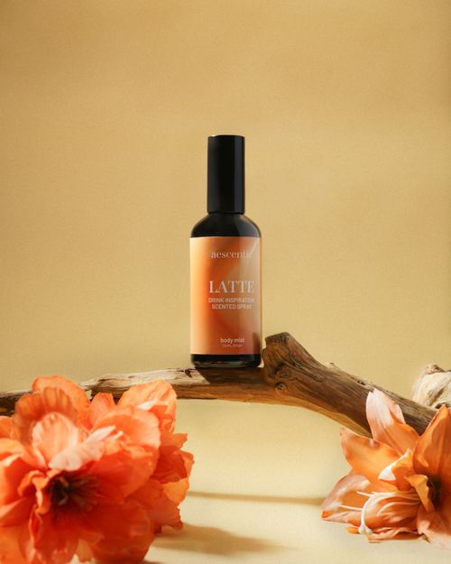 Free Elegant body mist bottle surrounded by bright orange flowers, displayed on natural wooden branch. Stock Photo