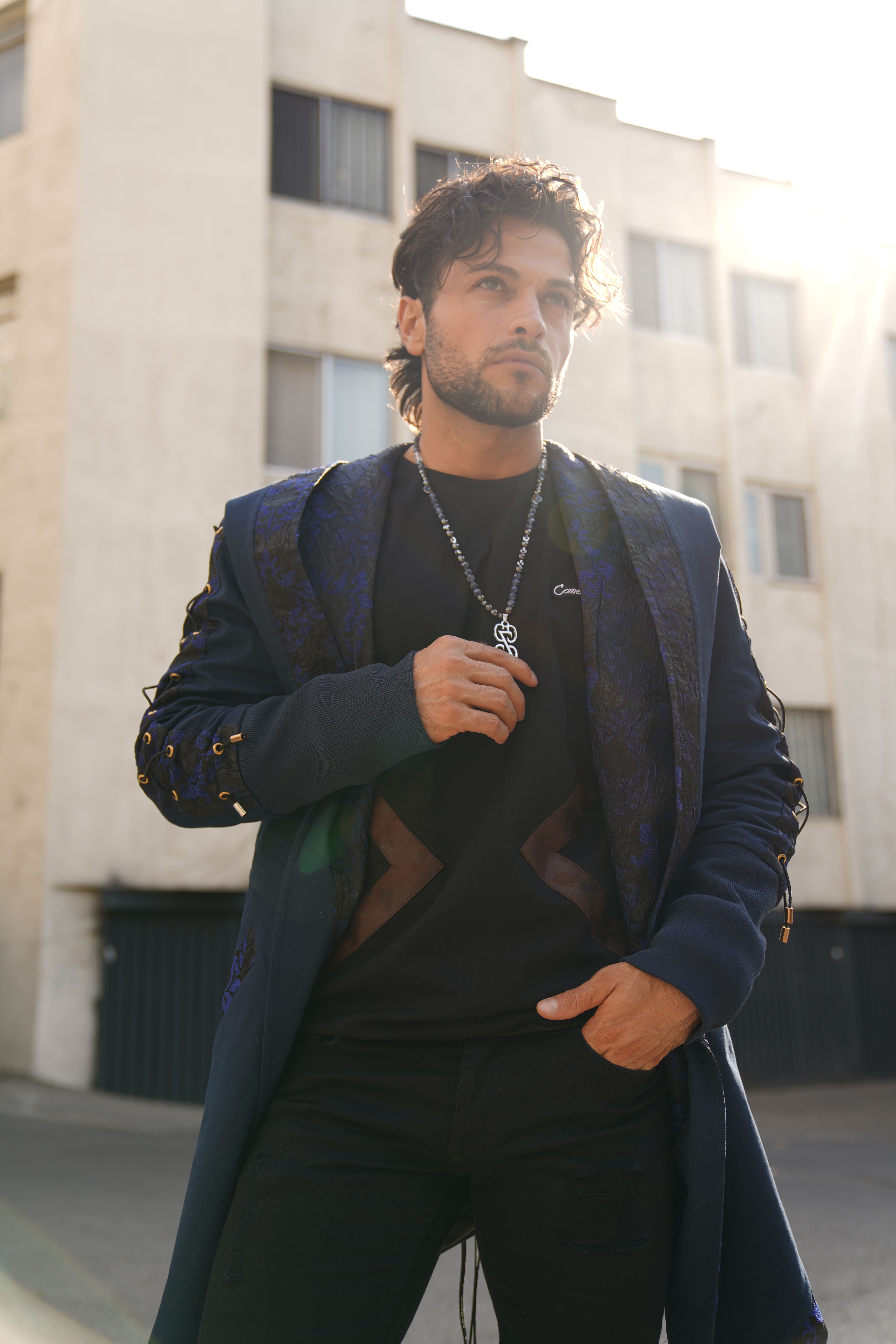 Fashionable man in a blue coat standing outside, illuminated by sunlight in Iran.