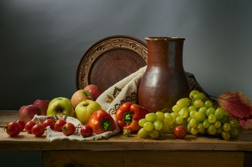 Free A classic still life composition featuring apples, grapes, and peppers arranged artfully with pottery. Stock Photo