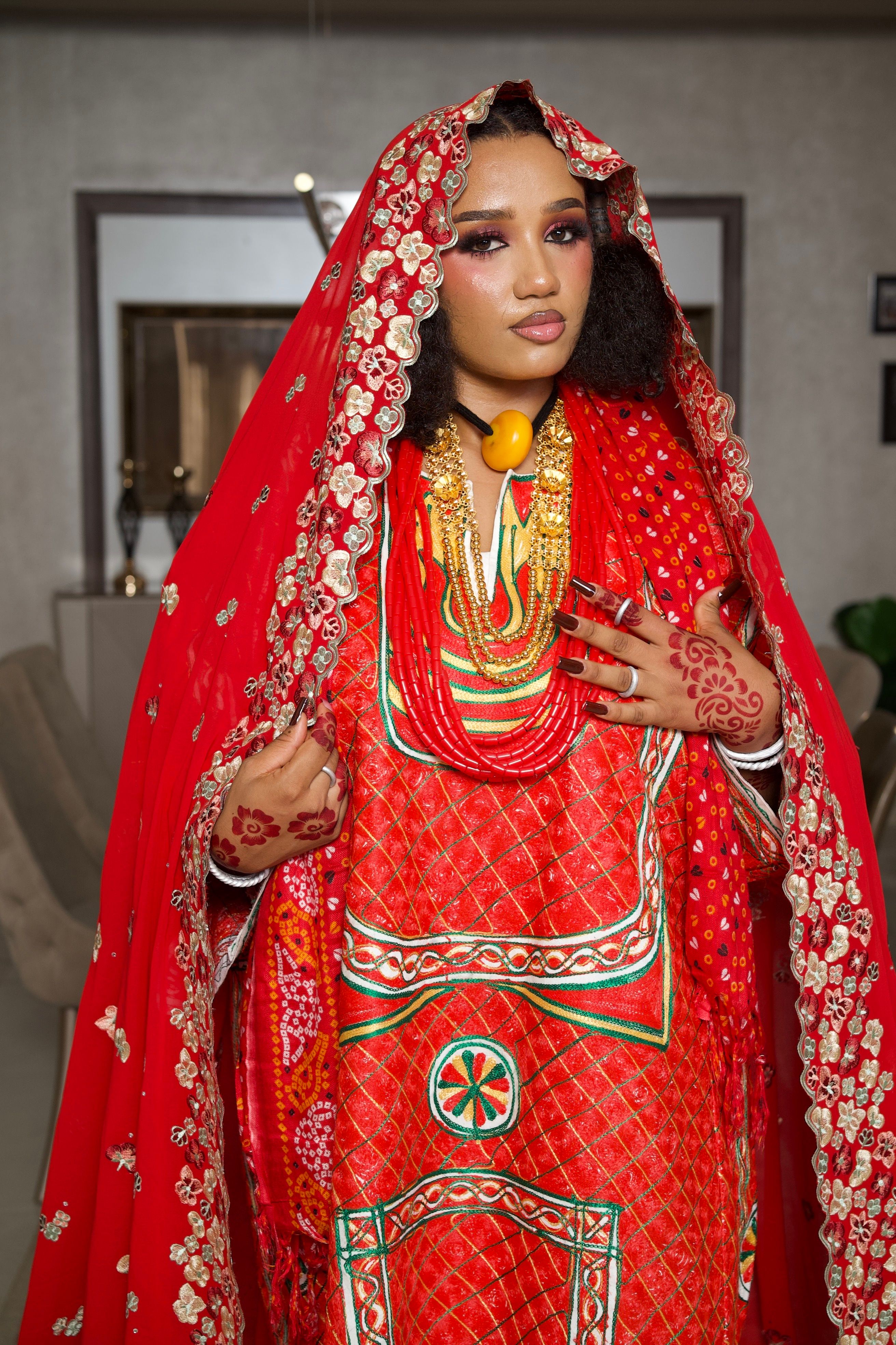 Stunning portrait of a Nigerian bride in a red traditional wedding dress with henna designs and gold jewelry.