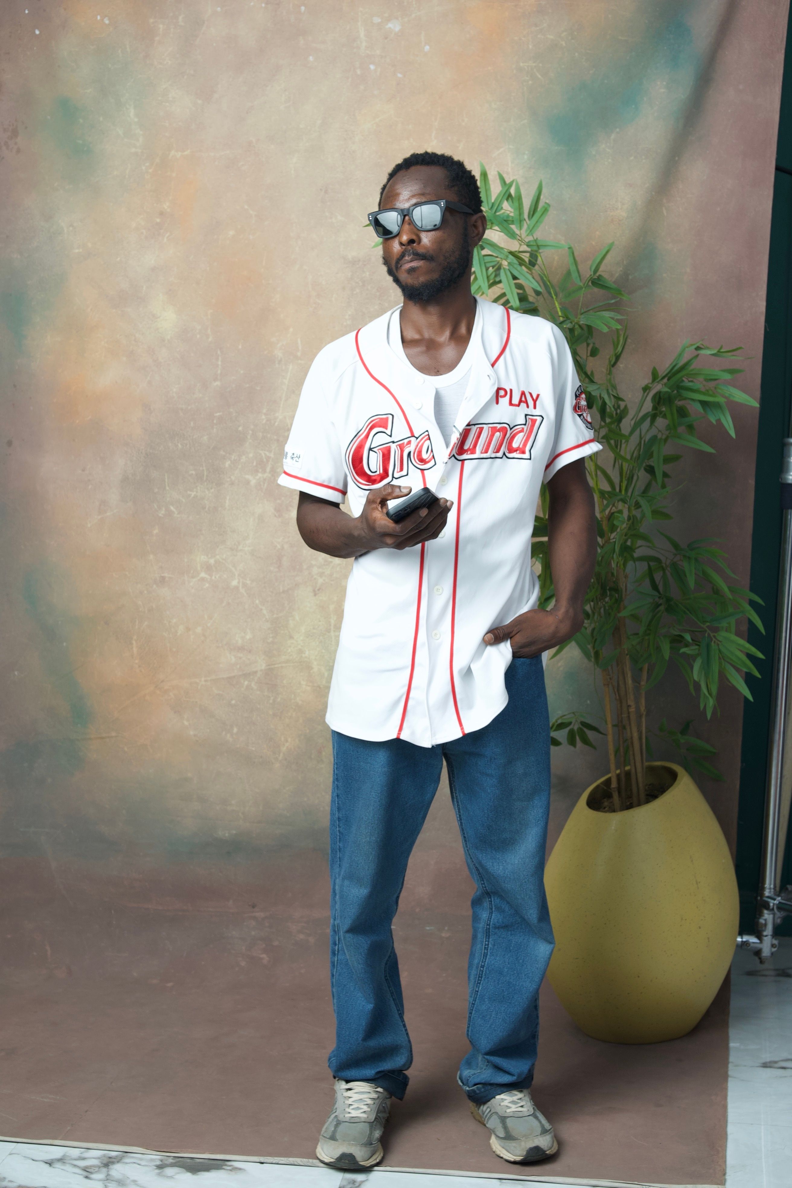 Casual portrait of a man in sunglasses and baseball jersey holding a smartphone.