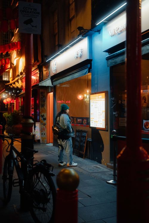 Free A person stands outside a lit restaurant in a vibrant Asian district at night. Stock Photo