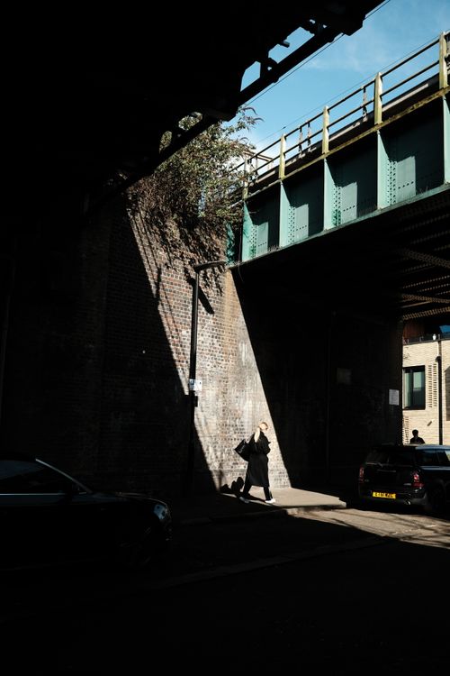 Free A person walks through sunlight under an urban bridge, casting deep shadows. Stock Photo
