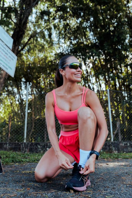 Free Smiling woman in sportswear tying shoelaces during a workout in a park under sunlight. Stock Photo