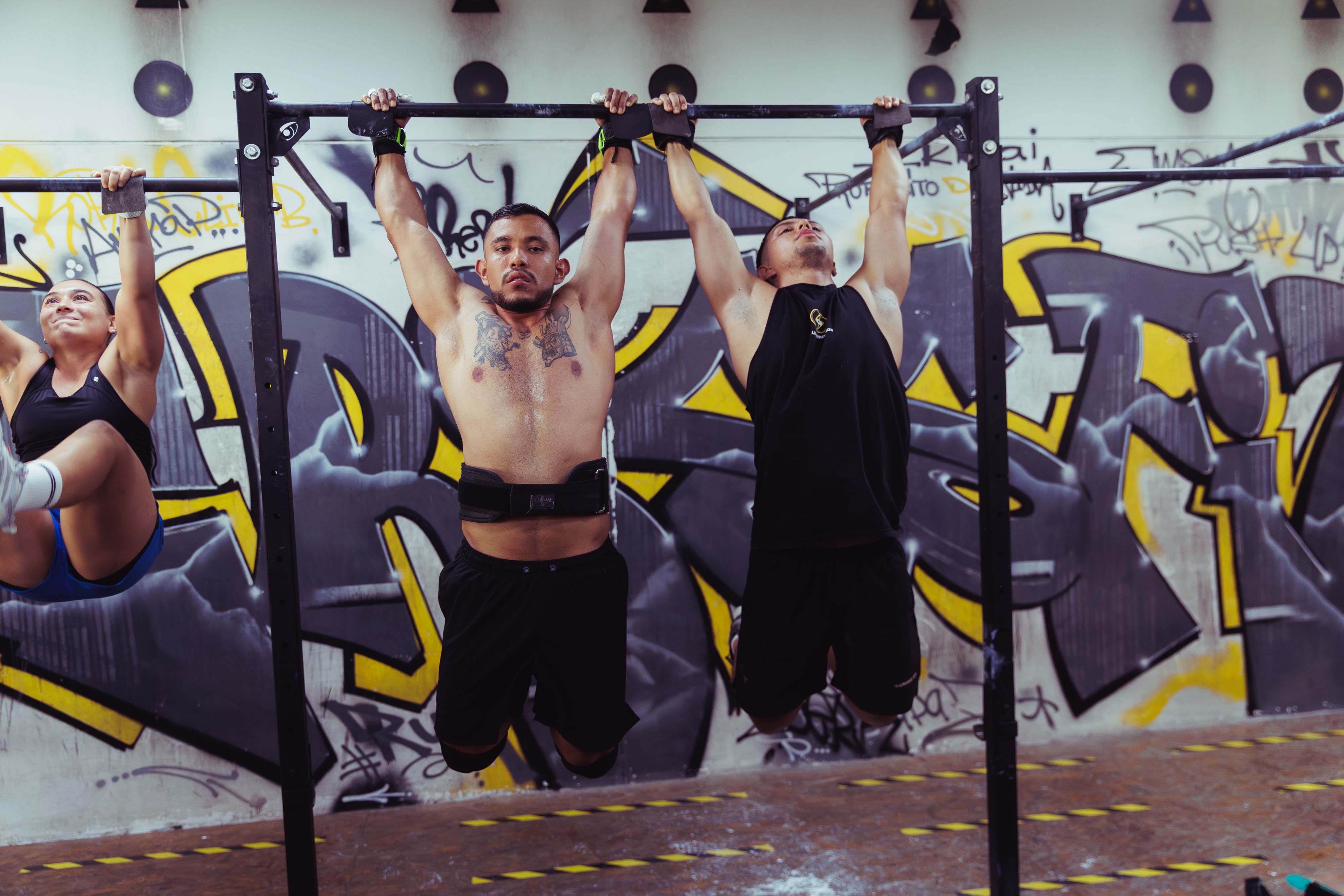 Group calisthenics session on pull-up bars in an urban graffiti-walled gym, community training energy
