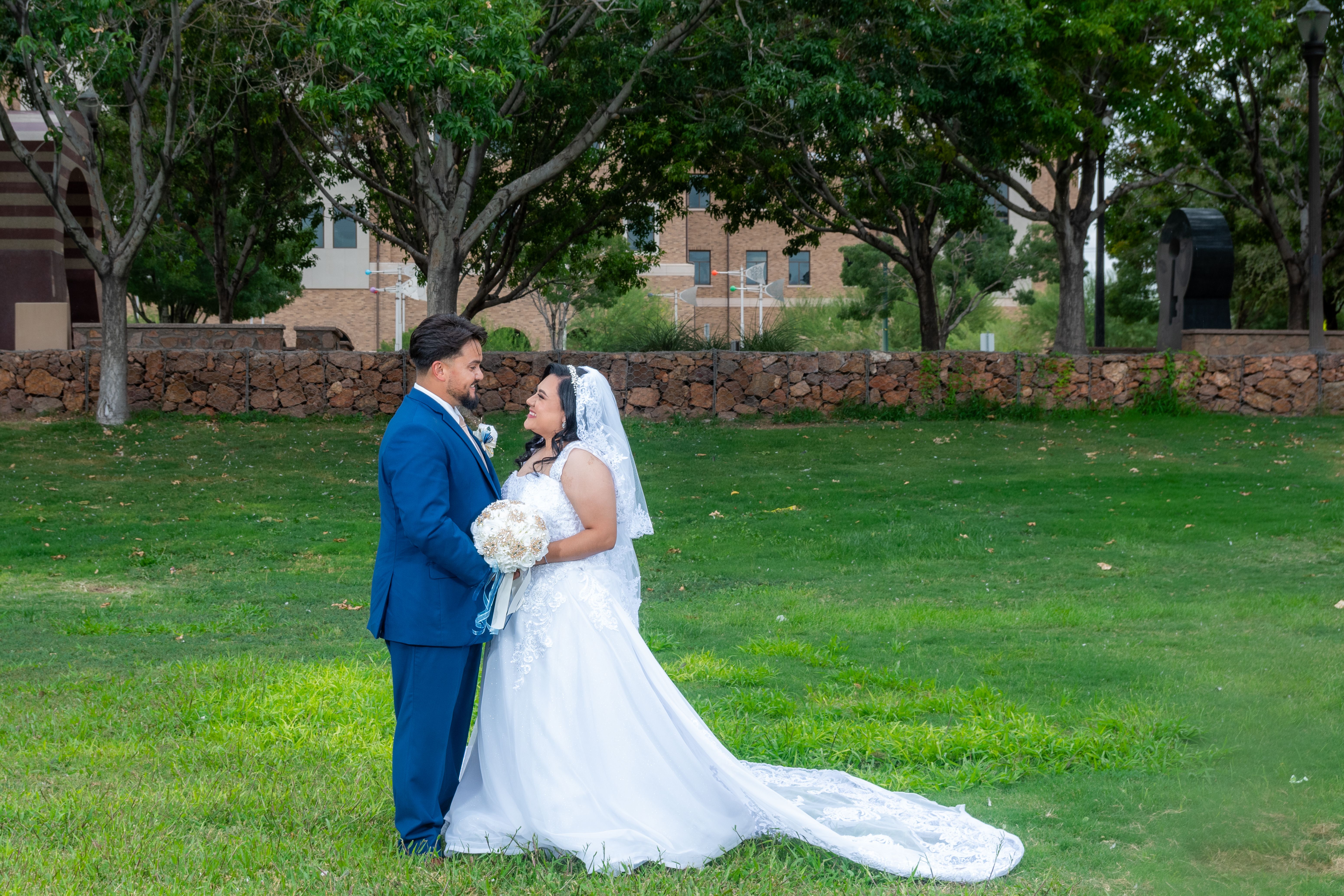 A joyful bride and groom standing together in an outdoor park setting under lush trees.