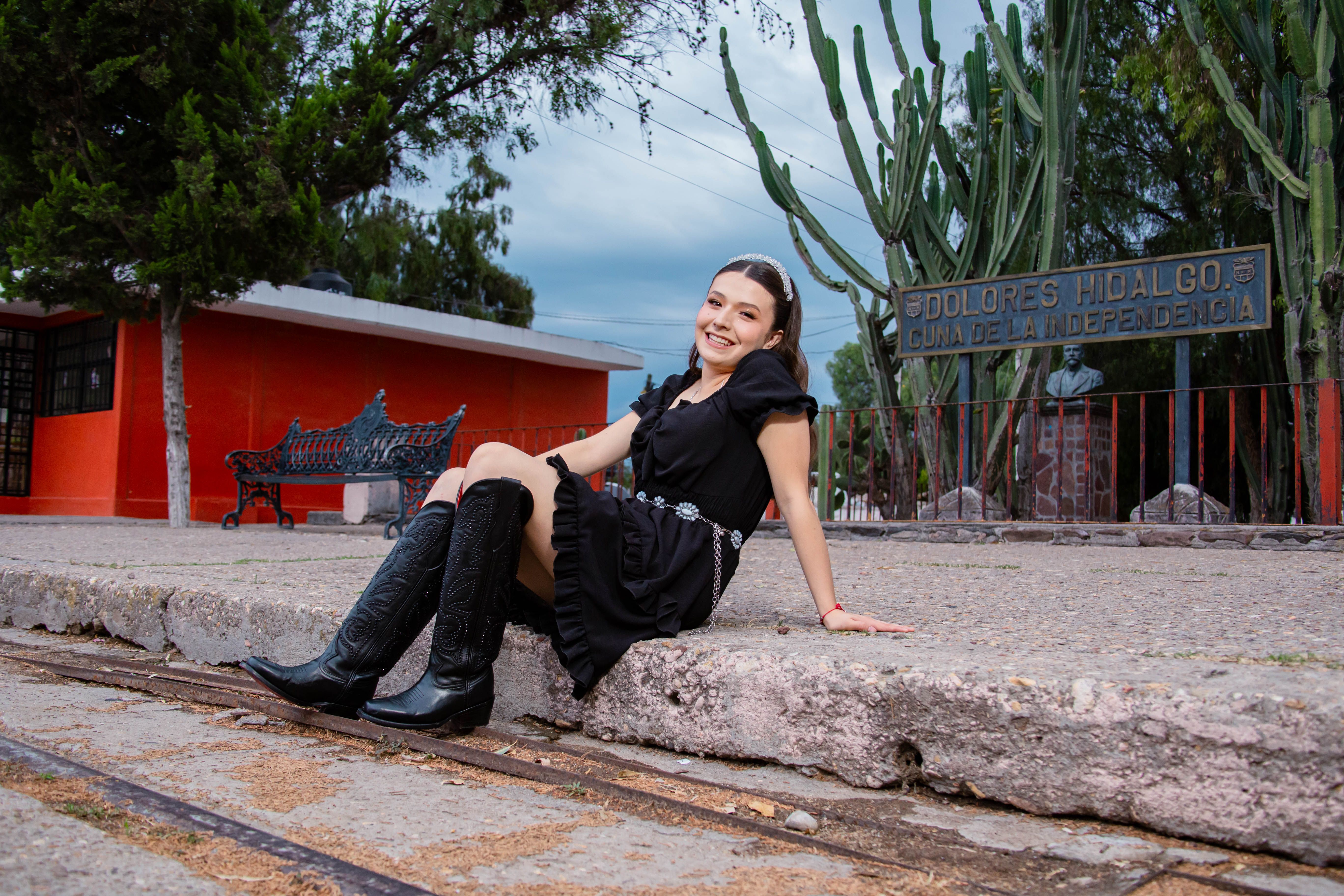 Young woman in black dress seated by Dolores Hidalgo sign, Gto., Mexico.