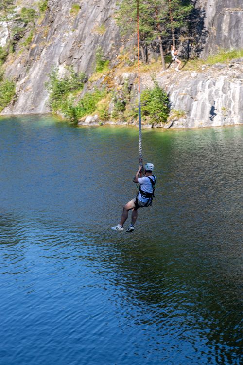 Free An adventurous person ziplining over a scenic lake surrounded by rugged cliffs and lush greenery. Stock Photo