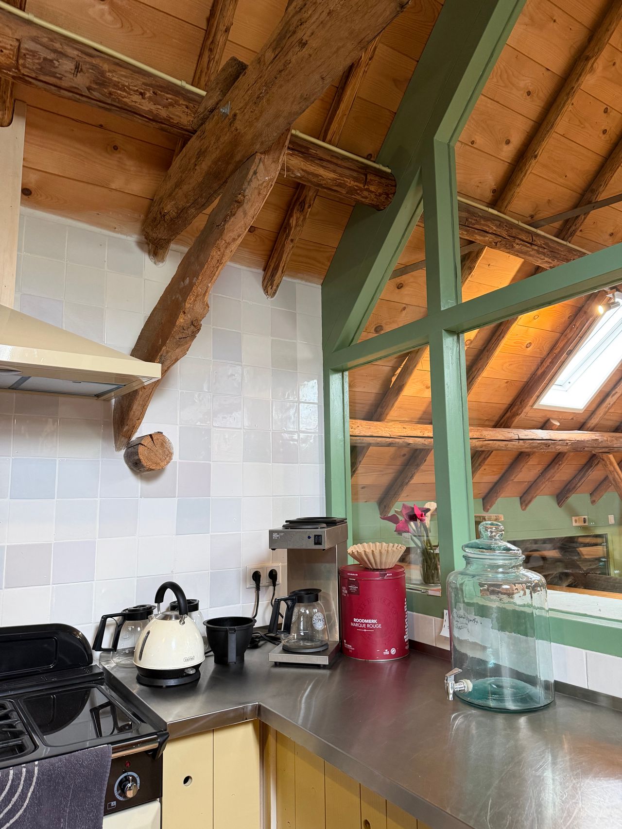 Rough exposed wooden beams across a wood plank ceiling in a rustic kitchen