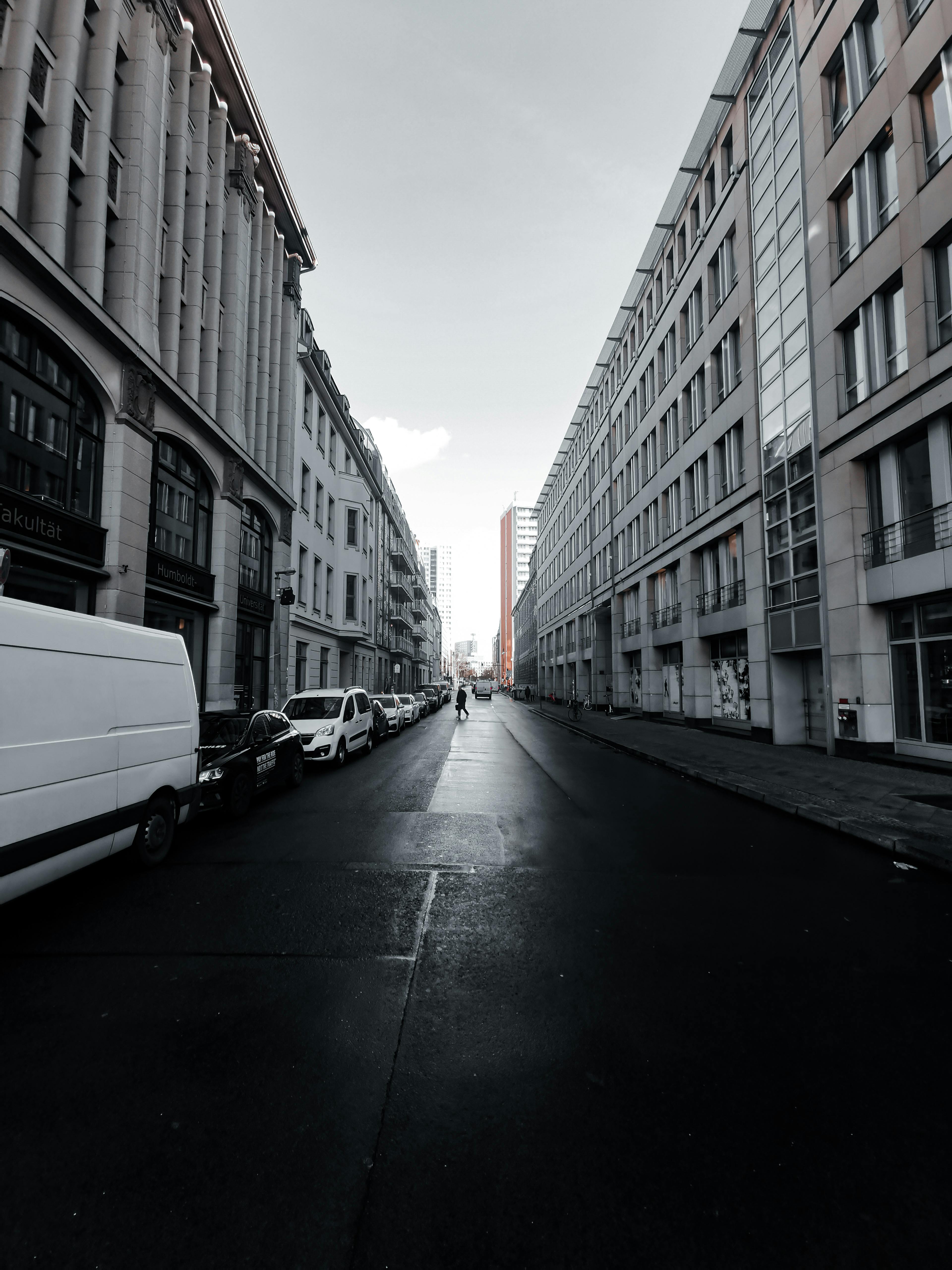 晴朗的天空下，城市街道两旁高楼林立，停着汽车