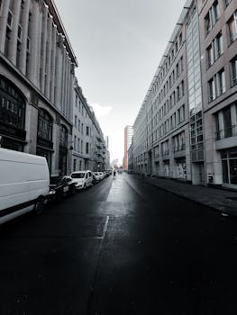 晴朗的天空下，城市街道两旁高楼林立，停着汽车