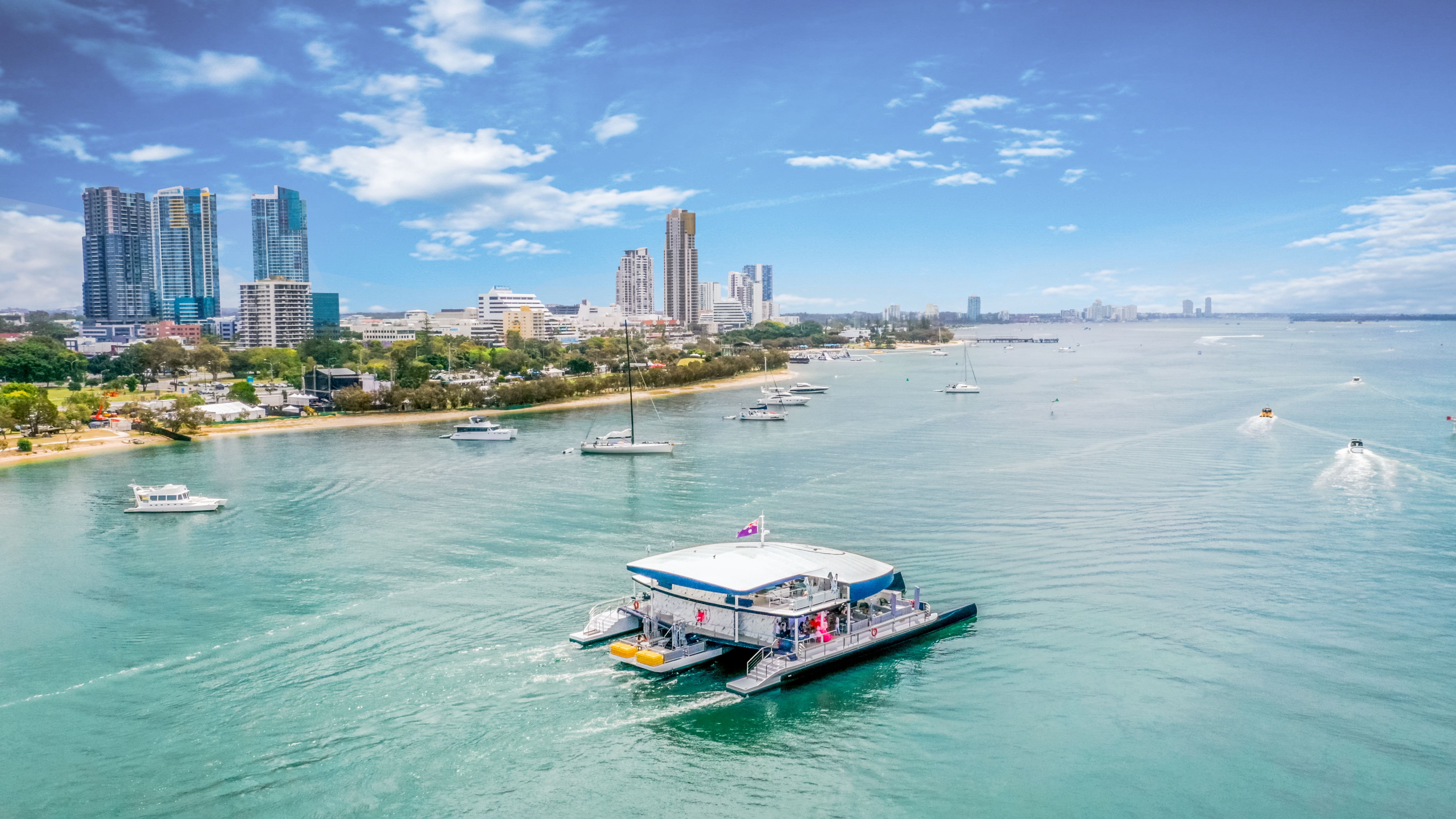 Boat moving across clear water toward a skyline of tall buildings.