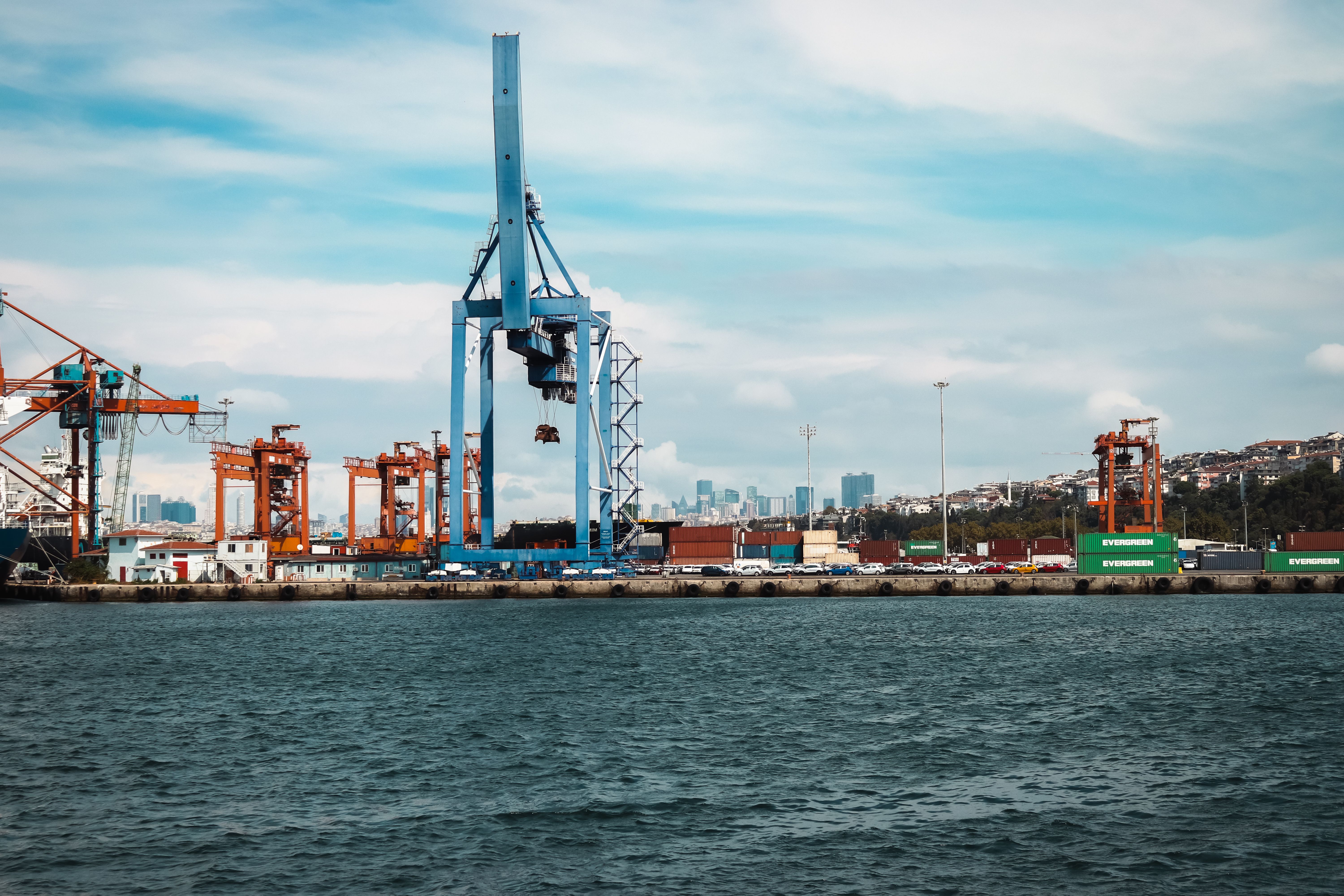 View of an industrial port in Istanbul with cranes and cargo containers against the city skyline.