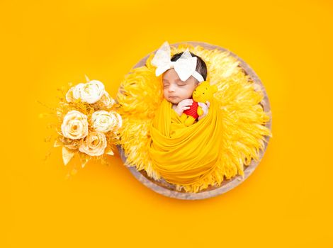 A sleeping newborn baby wrapped in yellow fabric, surrounded by yellow roses on a vibrant yellow background.