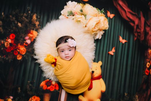 Cute newborn baby wrapped in yellow with stuffed toys and floral background.