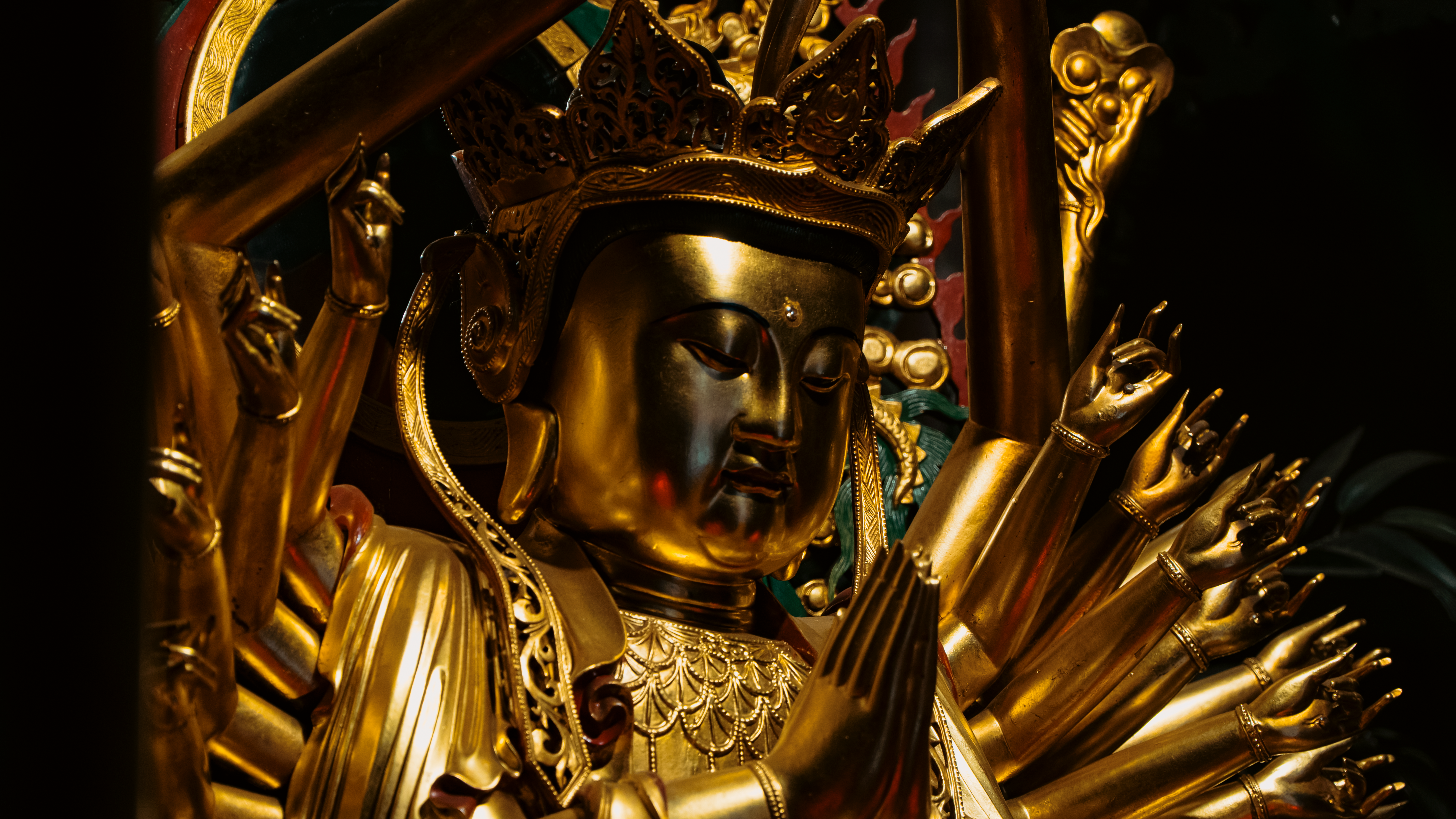 Intricate golden statue of a multi-armed Buddhist deity at a temple.