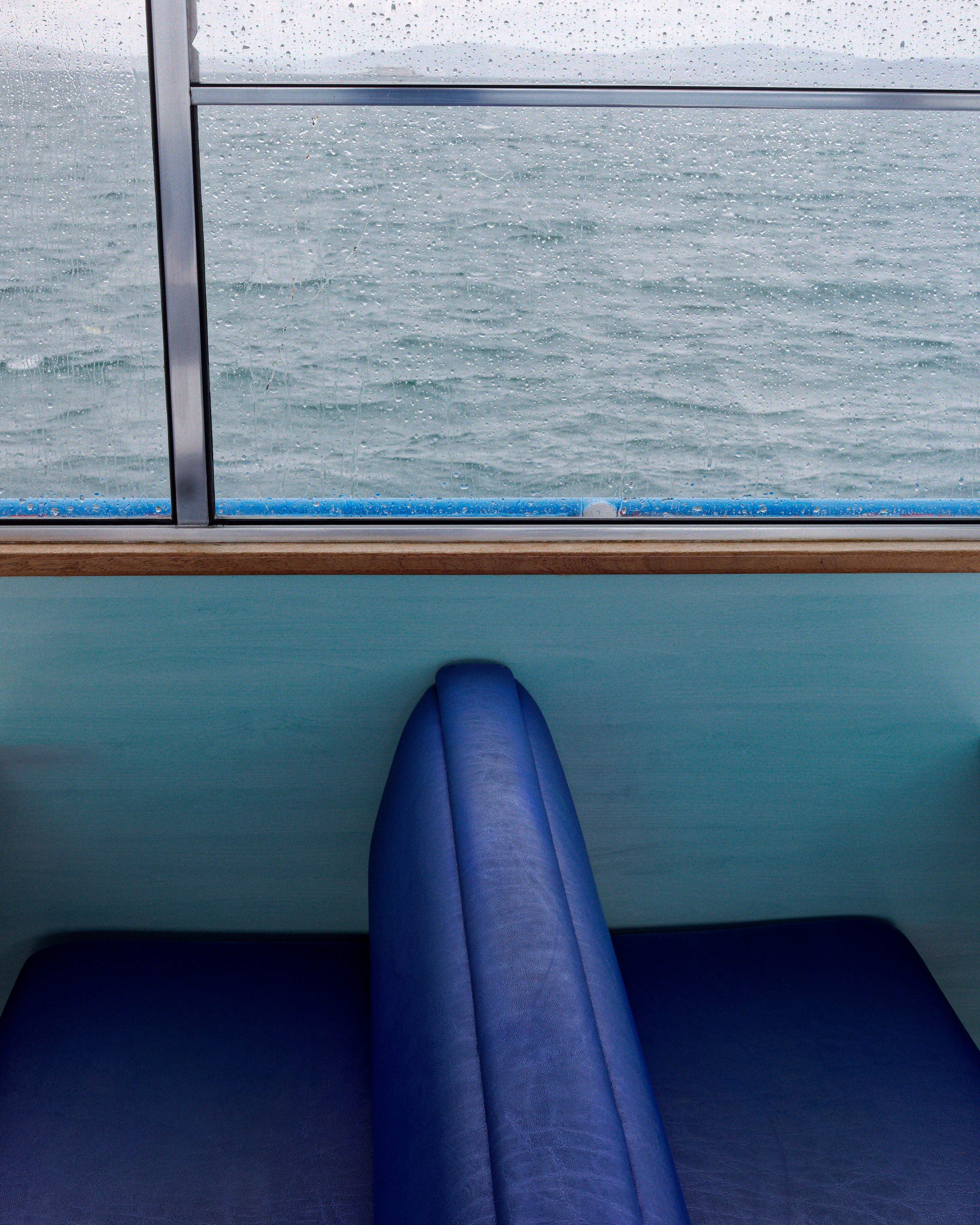 Blue seating against ocean view, seen from a raindrop-speckled window on a rainy day.