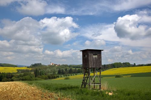 Free Beautiful countryside landscape with a church, wooden lookout, and expansive fields under a bright summer sky. Stock Photo