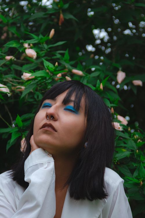 Free Asian woman with blue eye makeup and septum piercing in a lush garden setting. Stock Photo