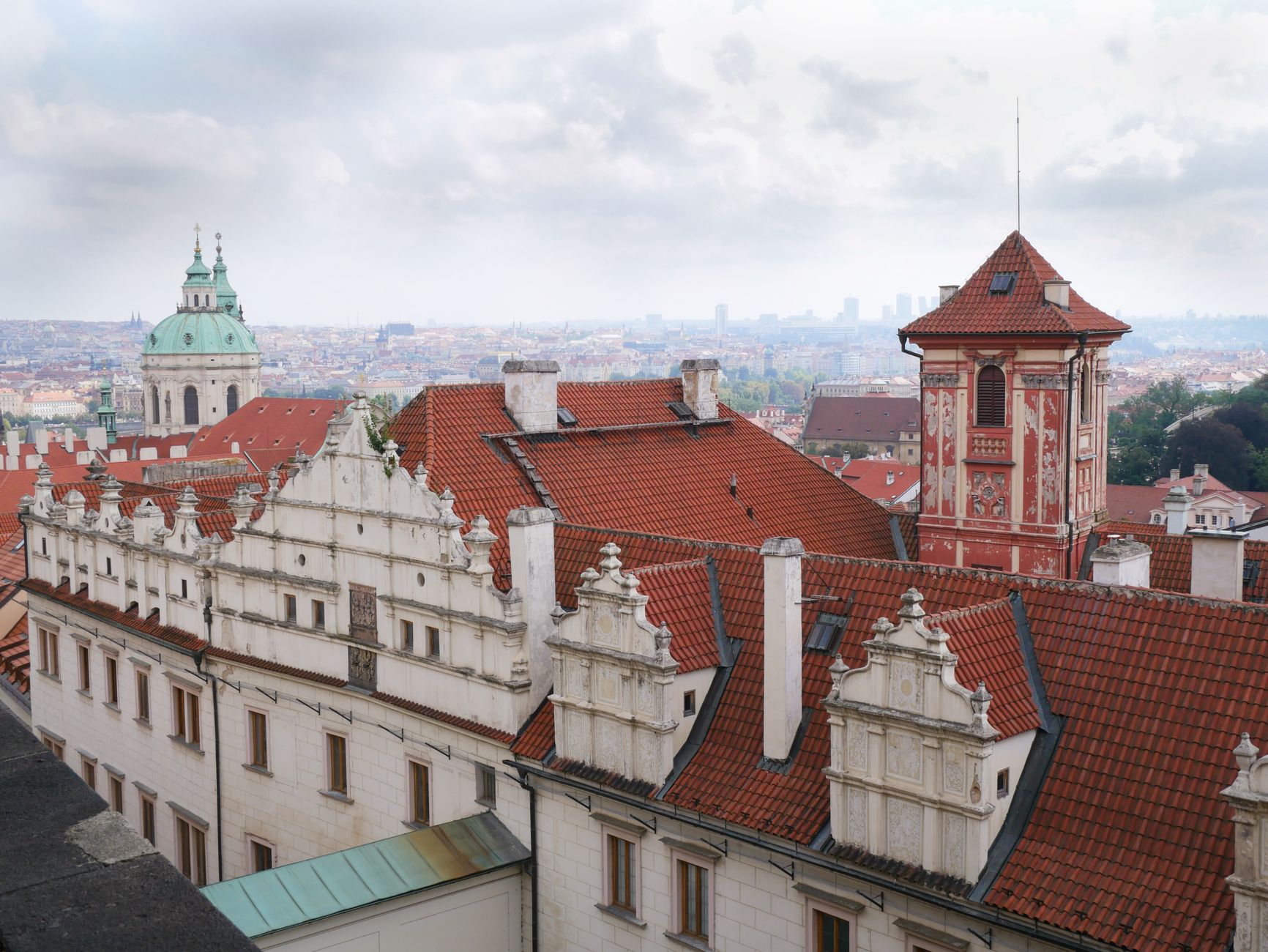 Elevated view of Prague's historic red rooftops and architectural landmarks under a cloudy sky.
