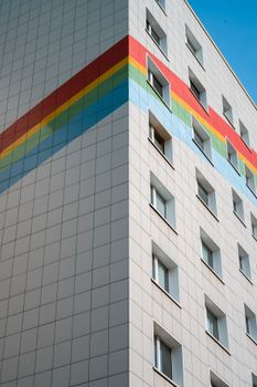 An urban apartment building features a distinctive rainbow stripe across its facade, enhancing modern architecture.