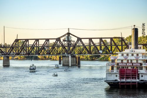 Free View of the Delta King Hotel and historic bridge over a river with small boats passing by. Stock Photo