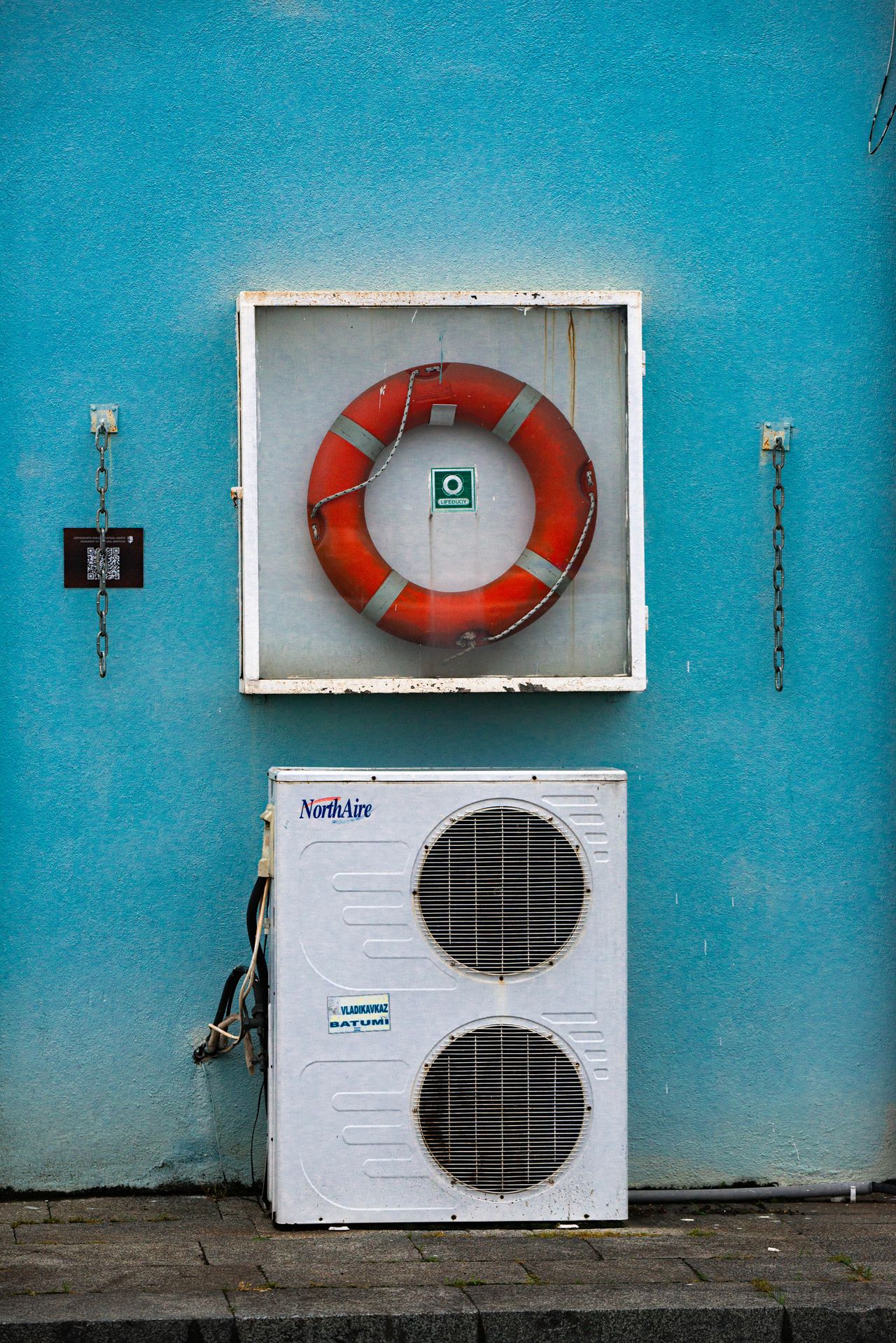 A white outdoor air conditioner unit mounted against a turquoise wall