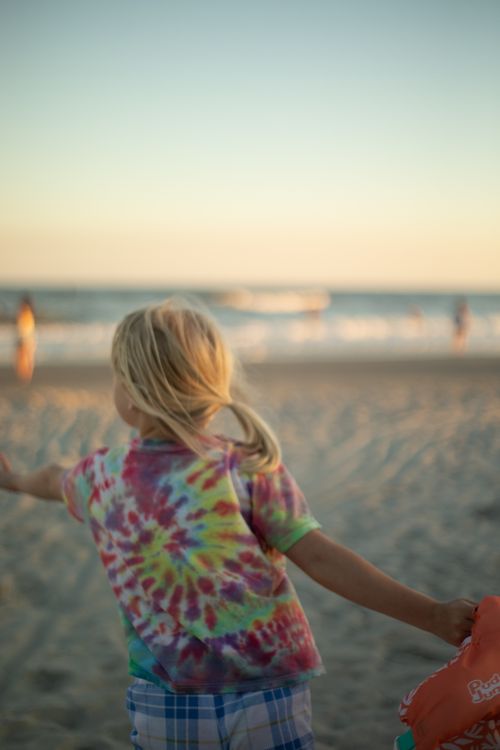 Free A child with a colorful shirt plays on Folly Beach, South Carolina, during a serene summer sunset. Stock Photo
