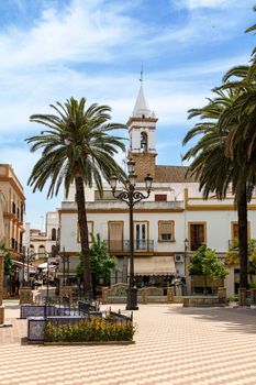 Sunny Spanish plaza with palm trees and historic buildings, capturing the essence of a Mediterranean town.