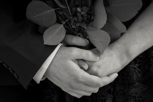 A close-up black and white image of a couple holding hands with green leaves. Captures intimacy and love.