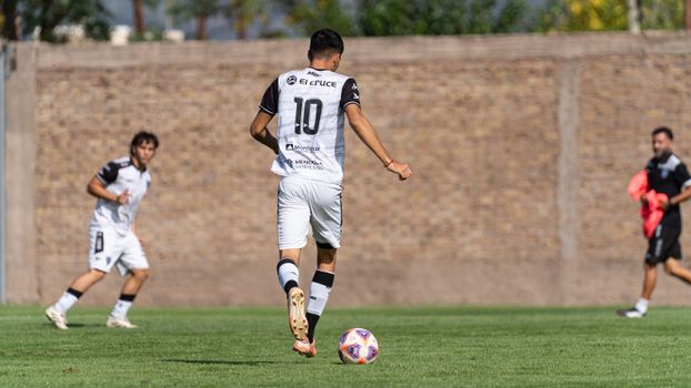 A soccer player wearing jersey number 10 dribbles the ball during a sunny outdoor match.