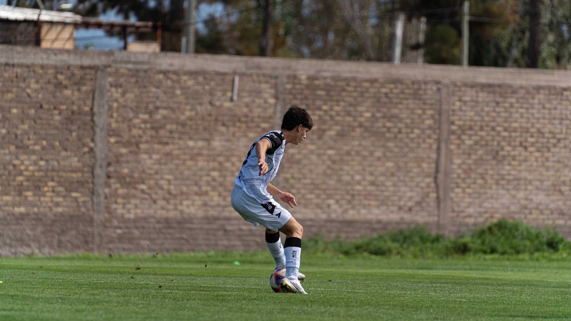 A young male soccer player skillfully dribbles the ball on an outdoor field.