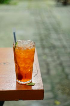 A glass of iced tea with ice cubes, placed on a wooden table outdoors, perfect for a refreshing break.