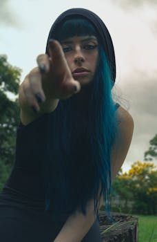 郁郁葱葱的户外环境中，一位蓝发伸手的女人肖像显得喜怒无常