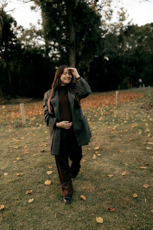 Free A woman in a coat enjoys a leisurely stroll in a park during autumn, surrounded by fallen leaves. Stock Photo